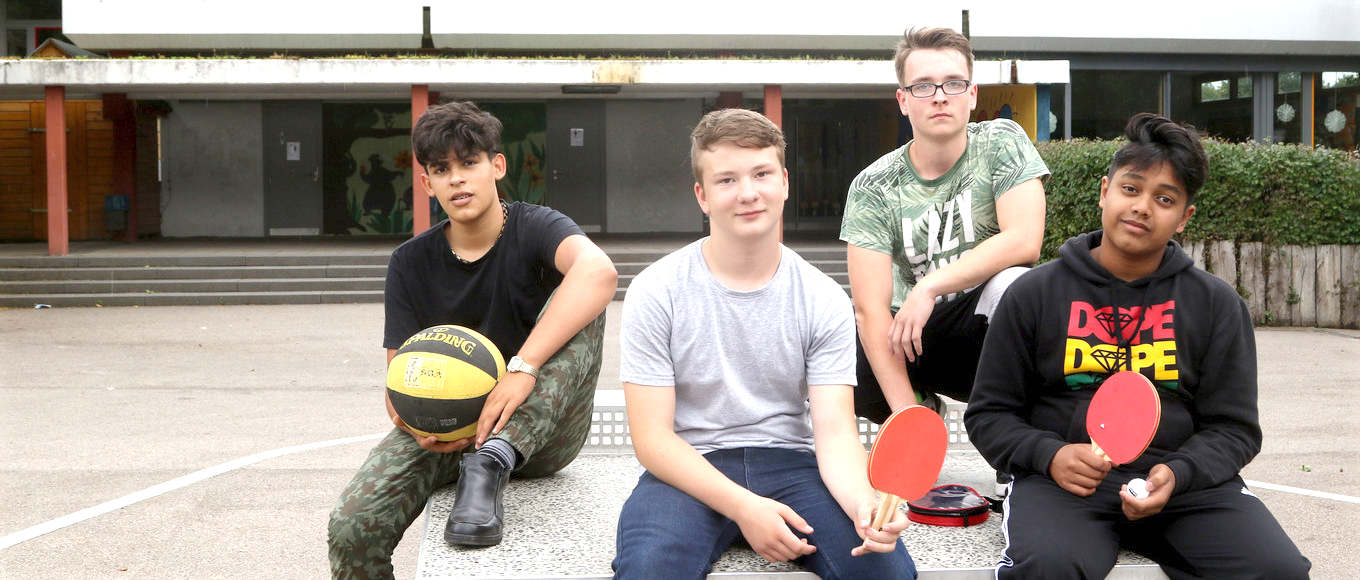 Vier Jugendliche mit Tischtennisschlägern vor dem Schulgebäude